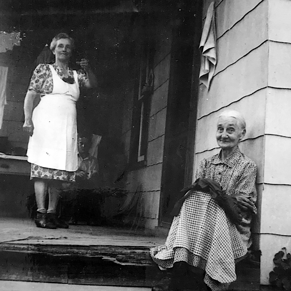 My grandmother Margie Reeder (standing on porch) and her mother (sitting).
